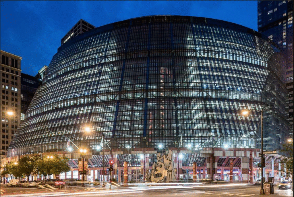 Evening view of Thompson Center’s curvilinear façade, principal entry and plaza with Dubuffet sculpture © Serhii Chrucky